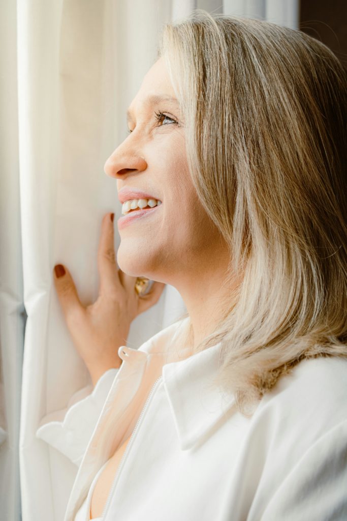 Bright portrait of a smiling woman gazing out the window, creating a feeling of hope and warmth.