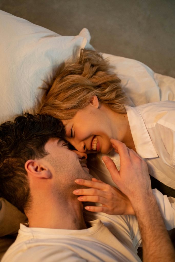 A loving couple lying down, sharing an intimate and joyful moment indoors.