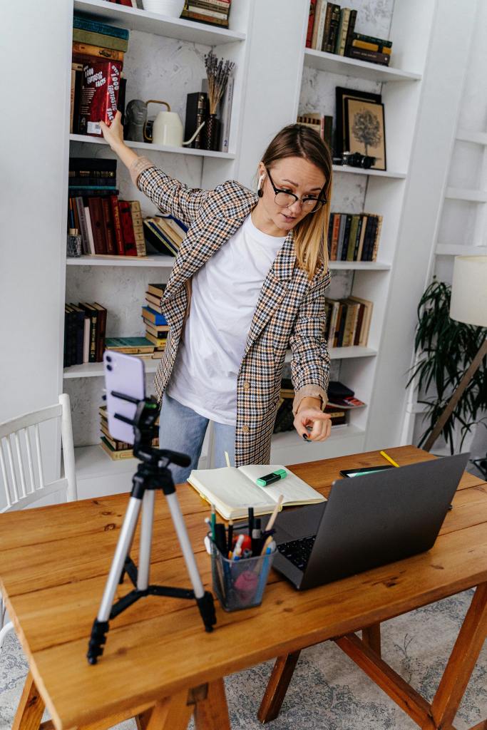 A woman conducting an online class from her home with a laptop and smartphone setup.